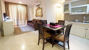 A compact living space with a dining area, a sofa, a kitchen with white cabinets, and a decorative mirror.