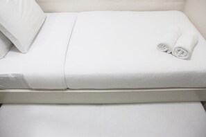 Una cama bien hecha con sábanas blancas y una toalla enrollada al lado.
