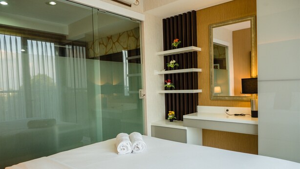 A hotel room with a bed, a glass shower enclosure, a vanity with a mirror, and a small shelf with flowers.
