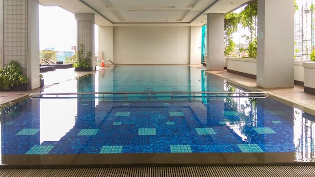 An indoor swimming pool with clear blue water, tiled floor, and a view of the cityscape through large windows. - Modern Studio The H Residence near MT Haryono (Jakarta)