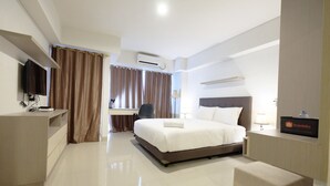A hotel room with a bed, a desk, a chair, a TV, and a minibar.