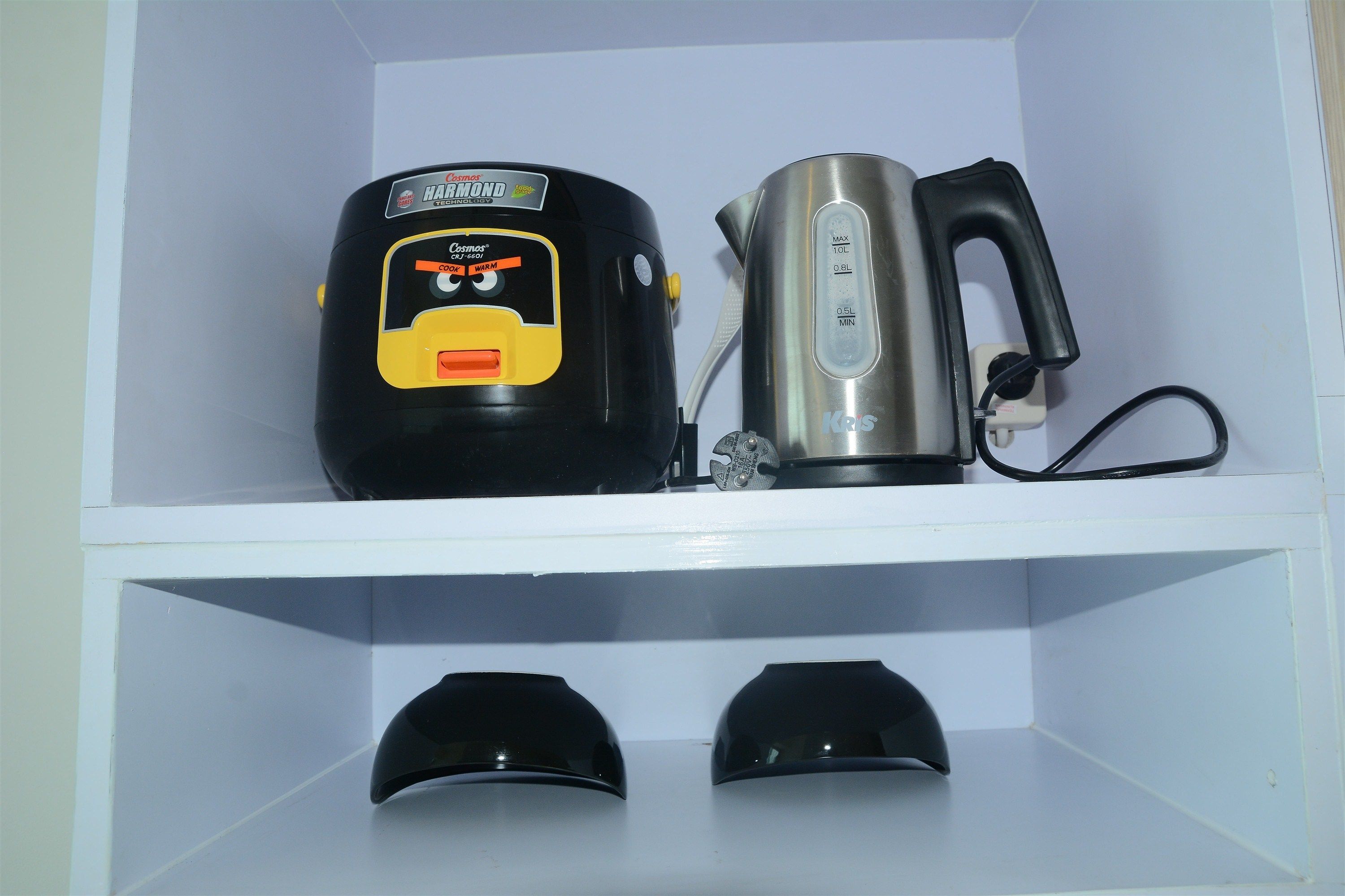 A kitchen with a black and yellow food processor, a silver kettle, and two black cups on the counter.