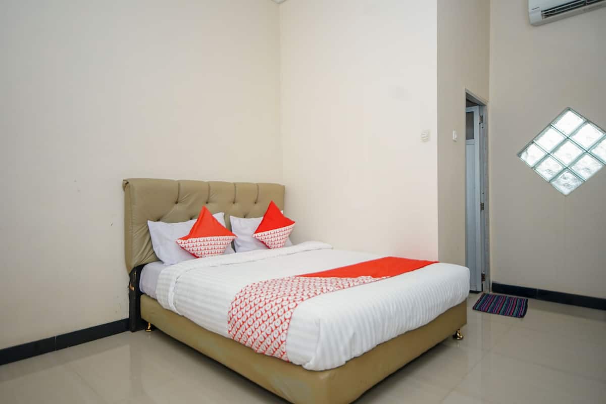 A neatly made bed with a beige headboard and white bedding, a small window, and a door in the background.