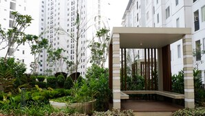 A modern building with a covered entrance, surrounded by lush greenery and tall residential buildings in the background. - Spacious 2BR Apartment Connected to Bassura City Mall (Jakarta)