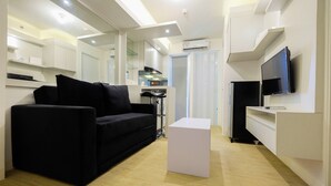 A modern living room with a black sofa, a white coffee table, and a flat-screen TV mounted on the wall. - Spacious 2BR Apartment Connected to Bassura City Mall (Jakarta)