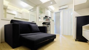 A modern living room with a black sofa, wooden flooring, and a kitchen area in the background. - Spacious 2BR Apartment Connected to Bassura City Mall (Jakarta)