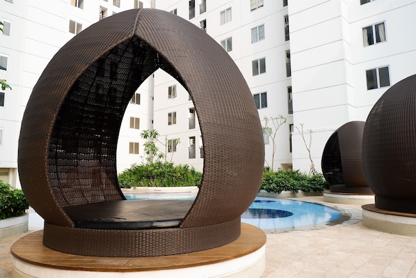 A modern outdoor seating area with a circular wicker design, a pool, and a multi-story building in the background.