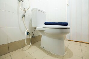 A white toilet with a blue towel on top, a white toilet paper holder, and a white flush handle.
