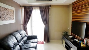 Un salon avec un canapé en cuir noir, un téléviseur fixé à un mur en bois et un tapis rouge.