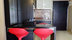 Une cuisine moderne avec un plan de travail noir, deux tabourets de bar rouges et un mur recouvert de carreaux.
