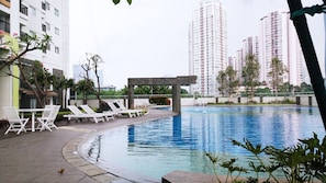 A swimming pool with lounge chairs and a pergola, surrounded by greenery and high-rise buildings. - Exclusive 1BR Apartment The Wave Kuningan near Epicentrum (Jakarta)