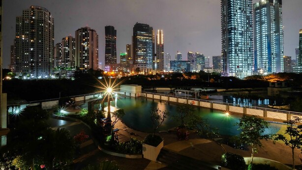 Une vue nocturne d’une ville, avec des gratte-ciel illuminés et un espace piscine doté de chemins et de coins salon.