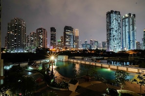 A nighttime cityscape with illuminated high-rise buildings and a swimming pool area with pathways and seating. - Exclusive 1BR Apartment The Wave Kuningan near Epicentrum (Jakarta)