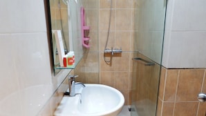 A bathroom with a white sink, a glass shower enclosure, and a pink towel rack. - Pool View Studio Apartment Tamansari Sudirman (Jakarta)