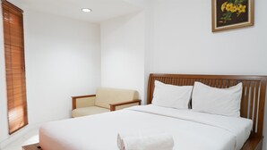 A neatly made bed with a rolled towel, a wooden headboard, and a chair with a cushion. - Pool View Studio Apartment Tamansari Sudirman (Jakarta)