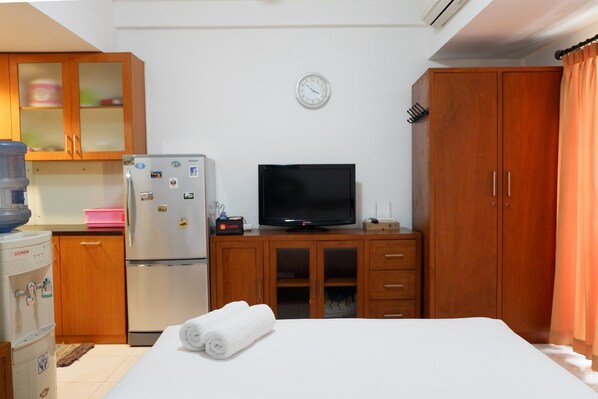 A hotel room with a bed, a television, a refrigerator, wooden cabinets, and a water dispenser.