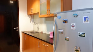 A kitchen with wooden cabinets, a stainless steel refrigerator, and a sink. - Pool View Studio Apartment Tamansari Sudirman (Jakarta)