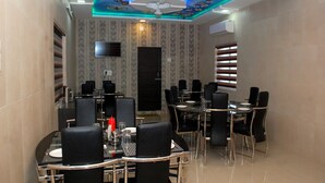 A restaurant with a ceiling mural, a flat-screen TV, and a black door. - Hotel Shree Pratham Milan (Nathdwara)