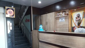 A hotel reception area with a wooden reception desk, a staircase, and a sign indicating check-out time. - Hotel Shree Pratham Milan (Nathdwara)