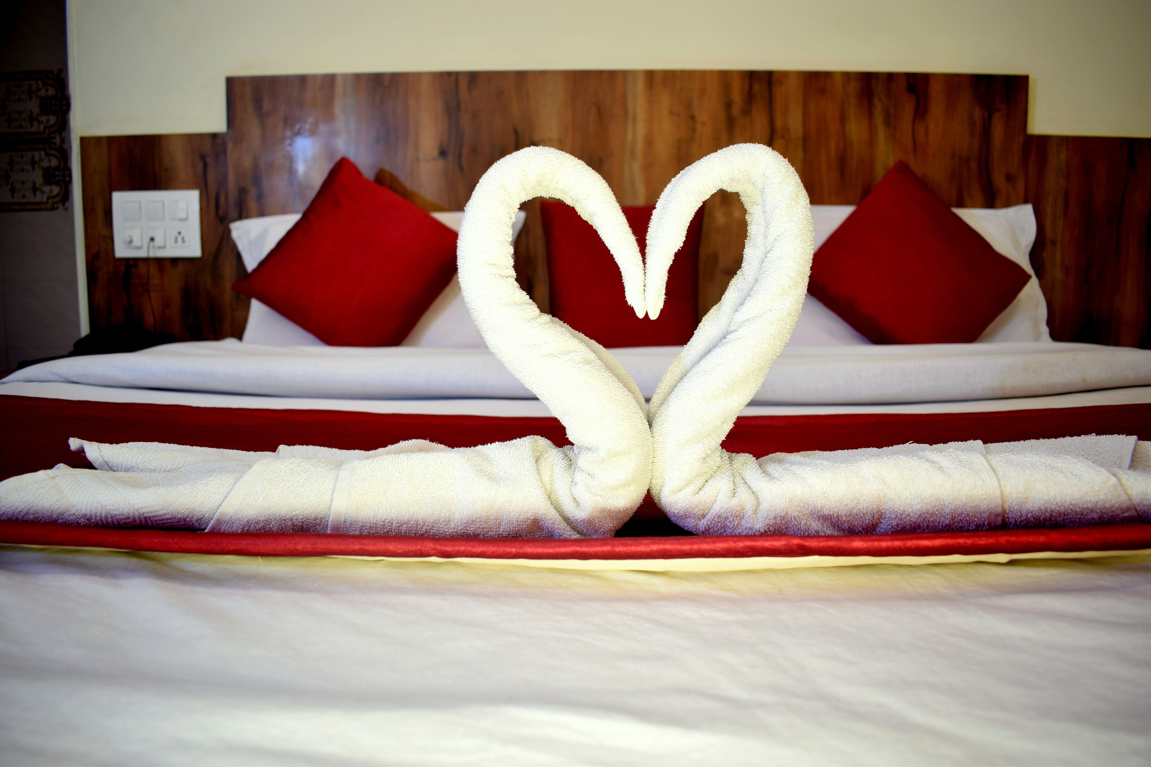 A bed with a heart-shaped towel arrangement and red pillows.