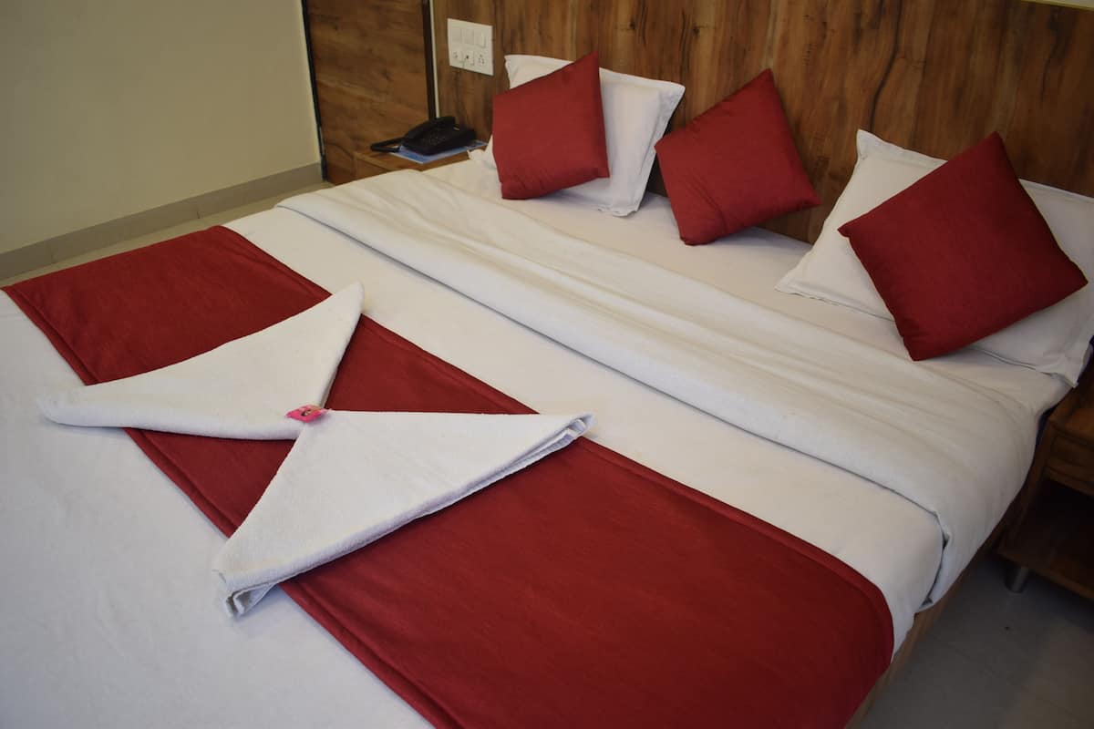 Uma cama bem arrumada com lençóis vermelhos e brancos, uma cabeceira de madeira e um telefone ao lado da cama.