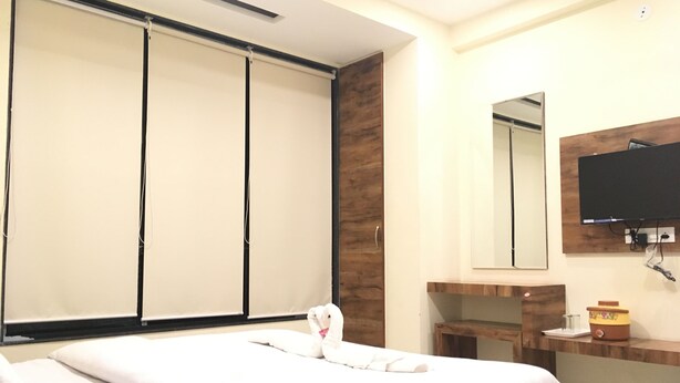 A hotel room with a bed, a wooden nightstand, a mirror, and a television. - Hotel Shree Pratham Milan (Nathdwara)