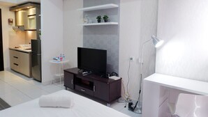 A modern hotel room with a flat-screen TV, a small round table, a white bed, and a desk area.