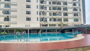 A modern hotel with a swimming pool, a covered area, and a staircase leading to the upper floors. - Comfy Studio Casa De Parco Apartment (Pagedangan)
