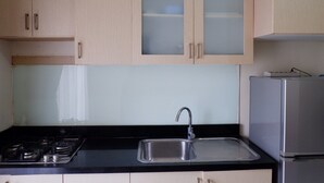 A kitchen with light wood cabinets, a stainless steel sink, a gas stove, and a refrigerator. - 2BR Apartment with City View at Mediterania Marina Residences (Jakarta)