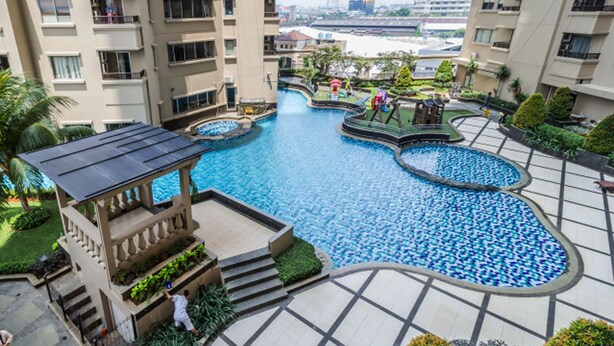 A multi-level residential building with a central swimming pool surrounded by greenery and a children's play area. - 2BR Apartment with City View at Mediterania Marina Residences (Jakarta)