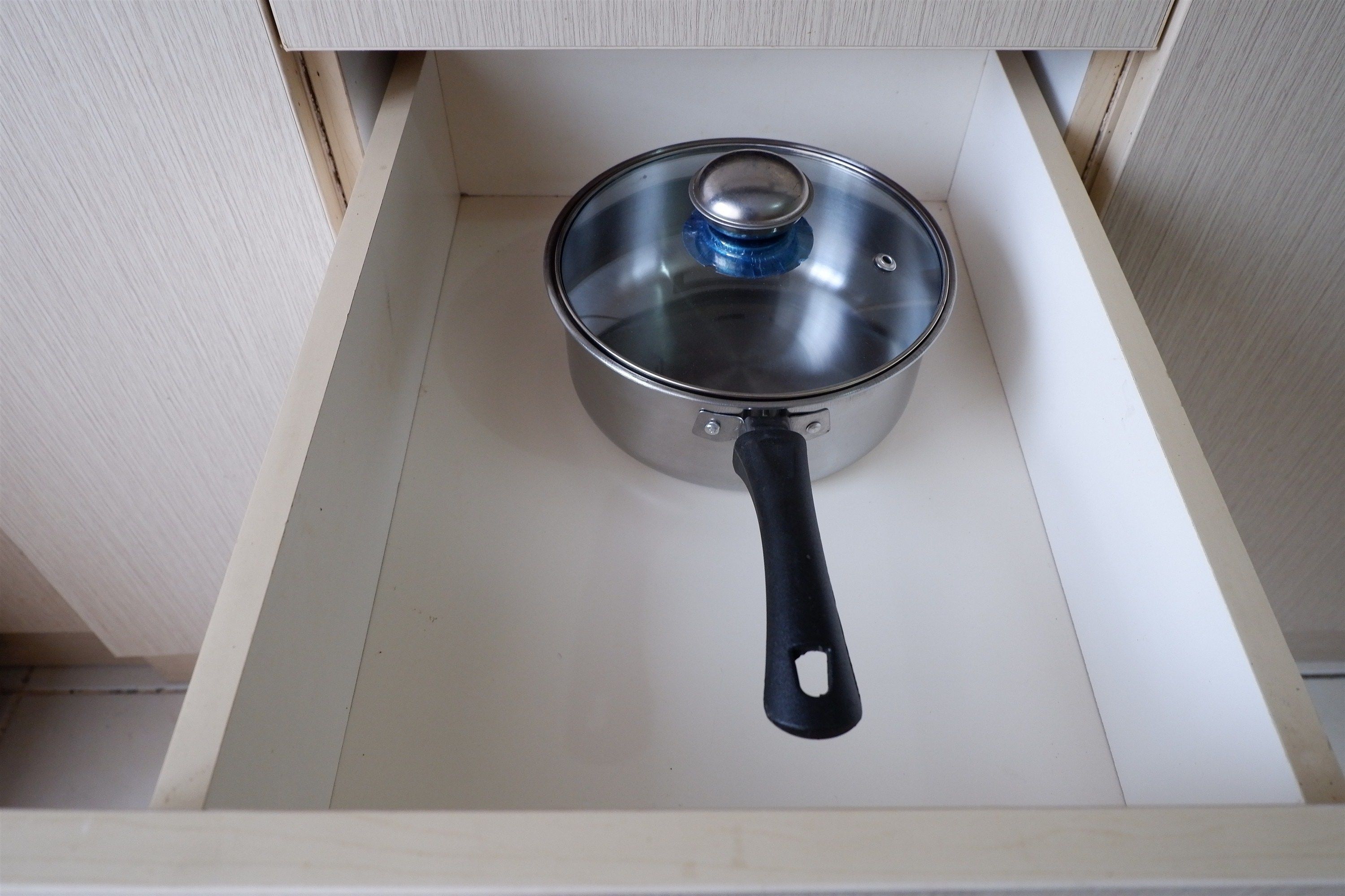 A kitchen drawer with a stainless steel pot with a black handle.