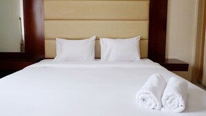 A neatly made bed with white linens and pillows, a wooden headboard, and two rolled white towels on the bed. - 2BR Apartment with City View at Mediterania Marina Residences (Jakarta)