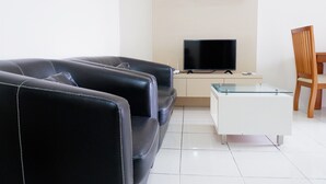 A living room with a black leather sofa, a glass coffee table, a television, and a wooden chair. - 2BR Apartment with City View at Mediterania Marina Residences (Jakarta)