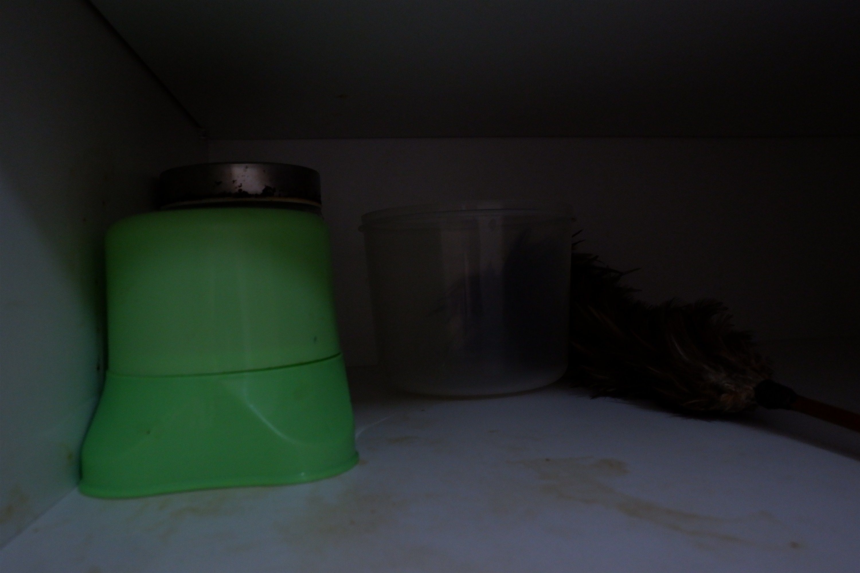 A green water bottle and a clear plastic container on a white surface.