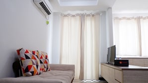 A modern hotel room with a sofa, a TV on a wooden cabinet, and a window with curtains. - Close to Pool Studio Apartment Sky Terrace at Daan Mogot Baru (Jakarta)
