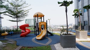 A playground with slides and a climbing structure, surrounded by landscaped areas and palm trees. - Close to Pool Studio Apartment Sky Terrace at Daan Mogot Baru (Jakarta)