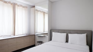 A hotel room with a bed, a bedside table, a mirror, and a window with curtains. - Close to Pool Studio Apartment Sky Terrace at Daan Mogot Baru (Jakarta)
