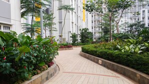 A paved pathway flanked by lush greenery and residential buildings.