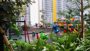 A playground with slides and climbing structures surrounded by greenery and tall buildings.