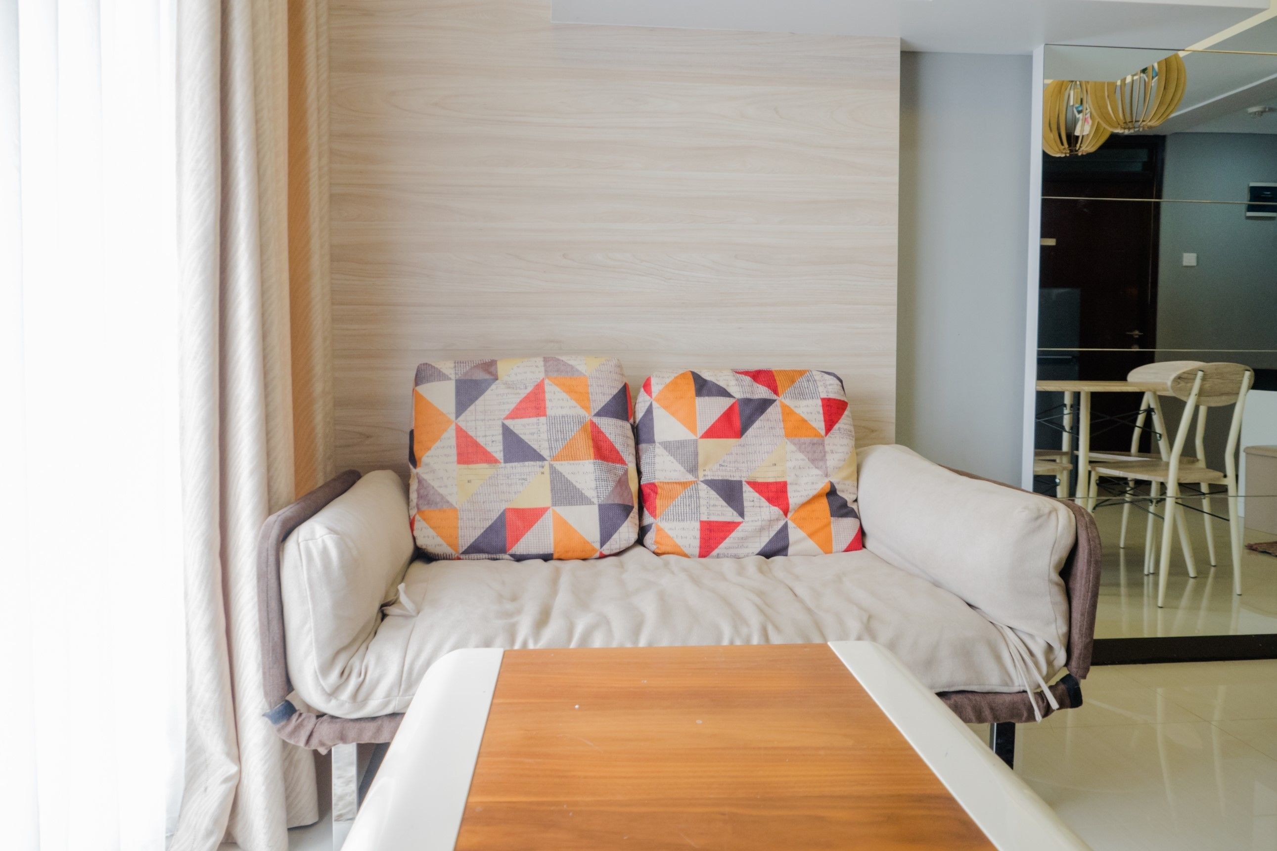 A modern living room with a sofa, two patterned cushions, a wooden coffee table, and a dining area in the background.