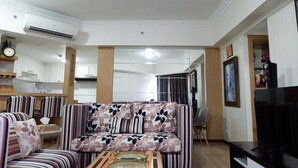 A living room with a sofa, armchairs, a TV, and a dining area with a chair and table. - Strategic 3BR Apt at Sudirman Tower Condominuim (Jakarta)