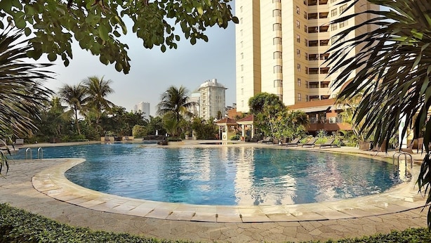 A swimming pool surrounded by palm trees and a tall building in the background. - Strategic 3BR Apt at Sudirman Tower Condominuim (Jakarta)