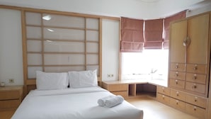 A bedroom with a large bed, a wooden wardrobe, a window with a view, and a bedside table. - Strategic 3BR Apt at Sudirman Tower Condominuim (Jakarta)