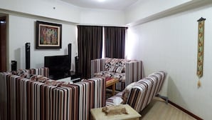 A living room with striped sofas, a television, and a framed picture on the wall. - Strategic 3BR Apt at Sudirman Tower Condominuim (Jakarta)