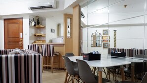 A dining area with striped upholstered booths, a white table with chairs, and a small bar area with a clock and decorative items. - Strategic 3BR Apt at Sudirman Tower Condominuim (Jakarta)