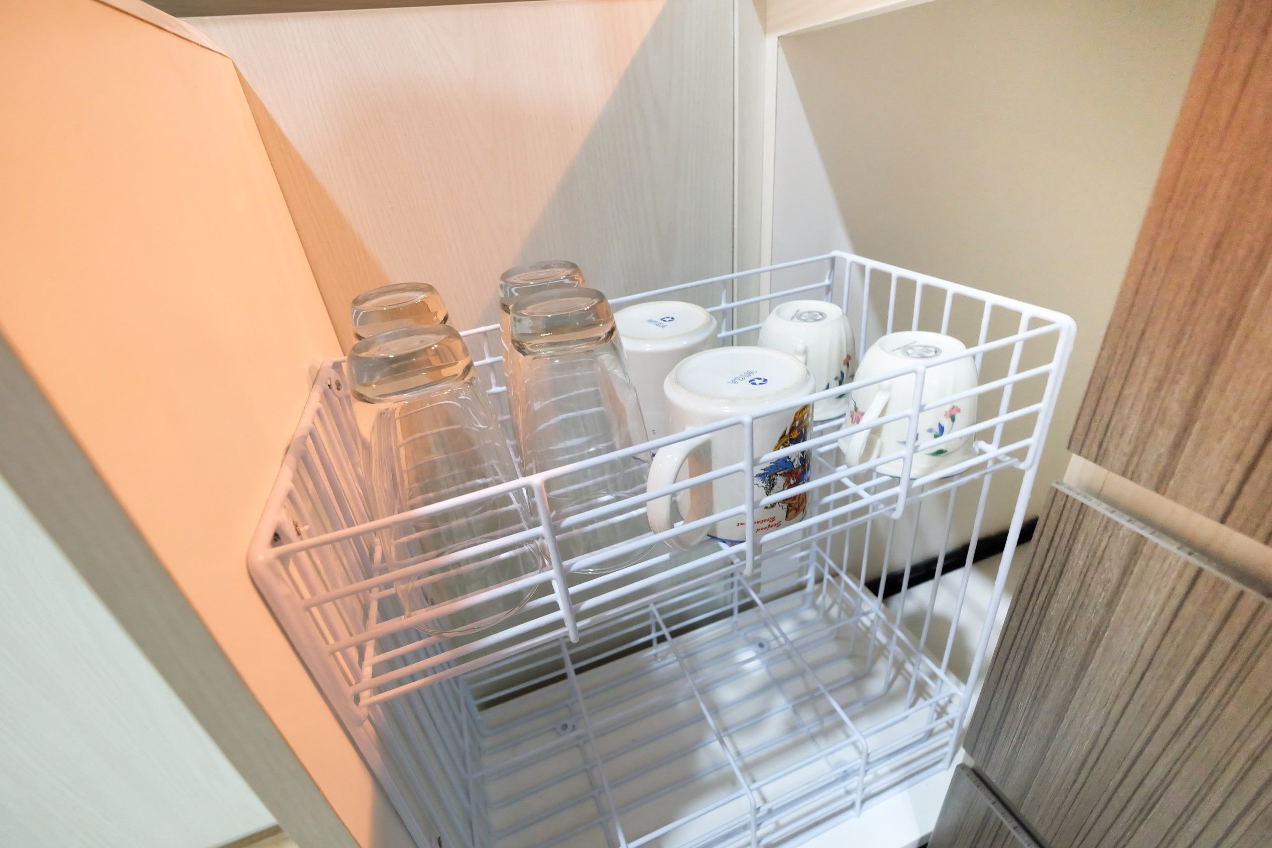 Un panier en fil métallique blanc contenant des bocaux en verre et des récipients blancs, placé dans un coin d’une pièce.