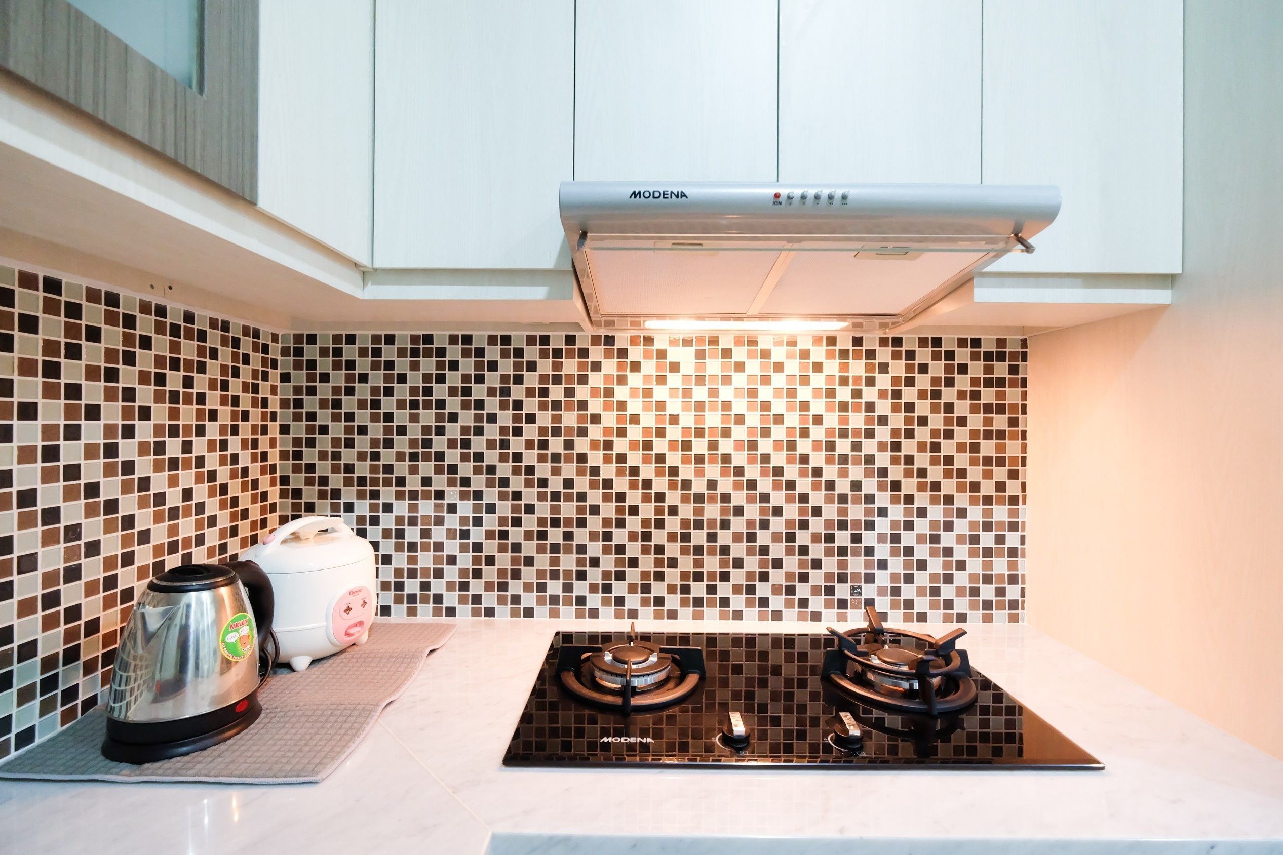 A kitchen with a black stove top, a kettle, and a rice cooker.