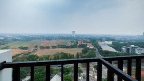 A view from a balcony overlooking a cityscape with a mix of green fields, roads, and buildings.