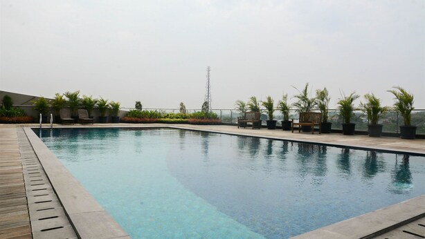 A rooftop pool with a wooden deck, surrounded by potted plants and a clear sky.