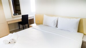 Quarto de hotel com cama, escrivaninha, cadeira e espelho.